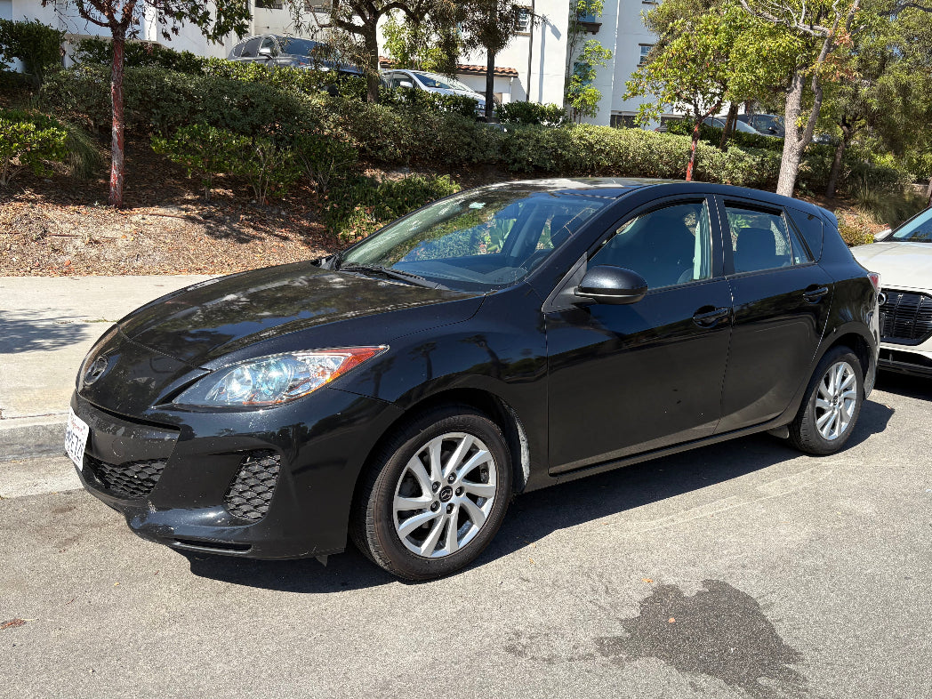 Black car parked on a street with trees and buildings in the background