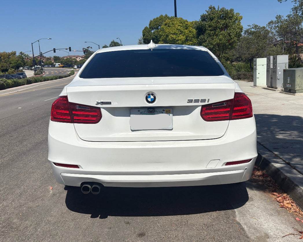 White BMW car parked on the side of a road with trees and power boxes in the background.