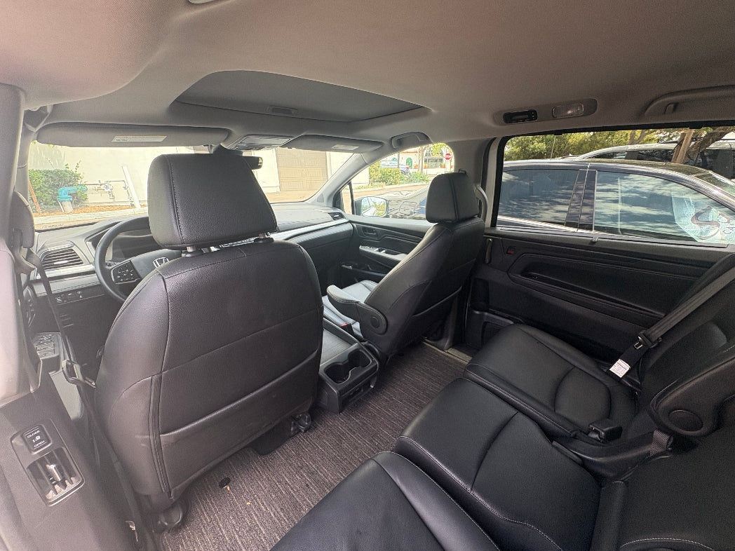 Interior of a vehicle with gray seats and a suitcase on the floor.
