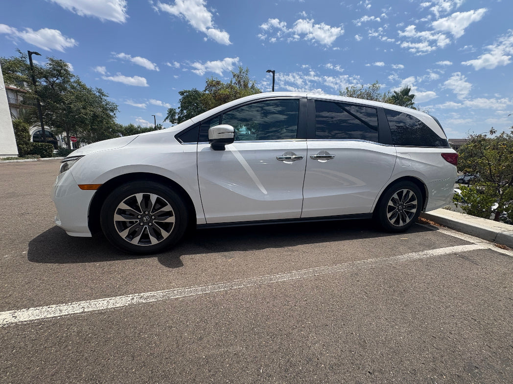White minivan parked in a parking lot with trees and blue sky in the background