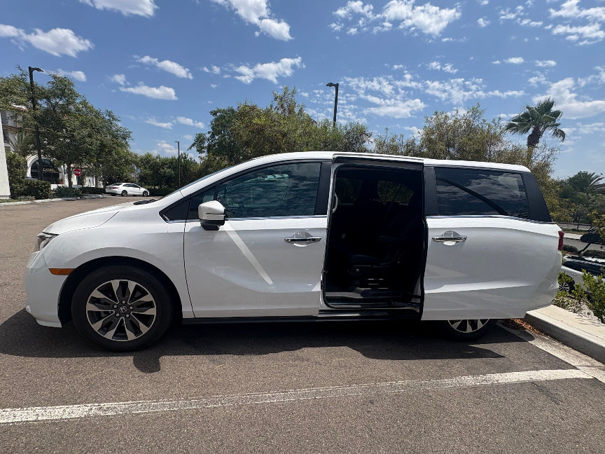 White minivan with open door in a parking lot under a blue sky.