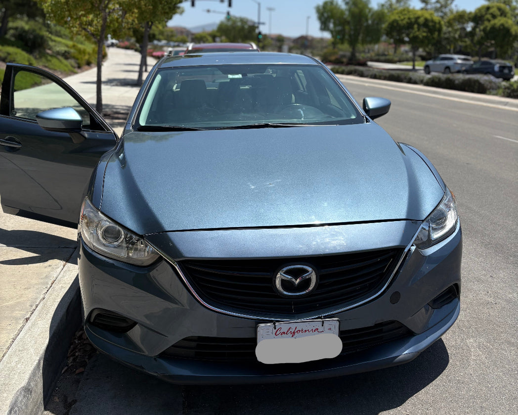 Blue Mazda car parked on the side of a road with trees and clear sky in the background
