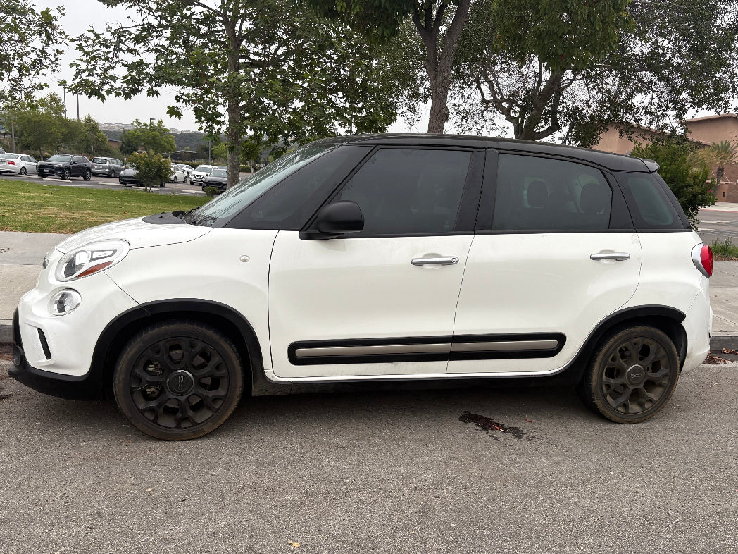 White SUV with black rims parked on a paved surface with trees and buildings in the background