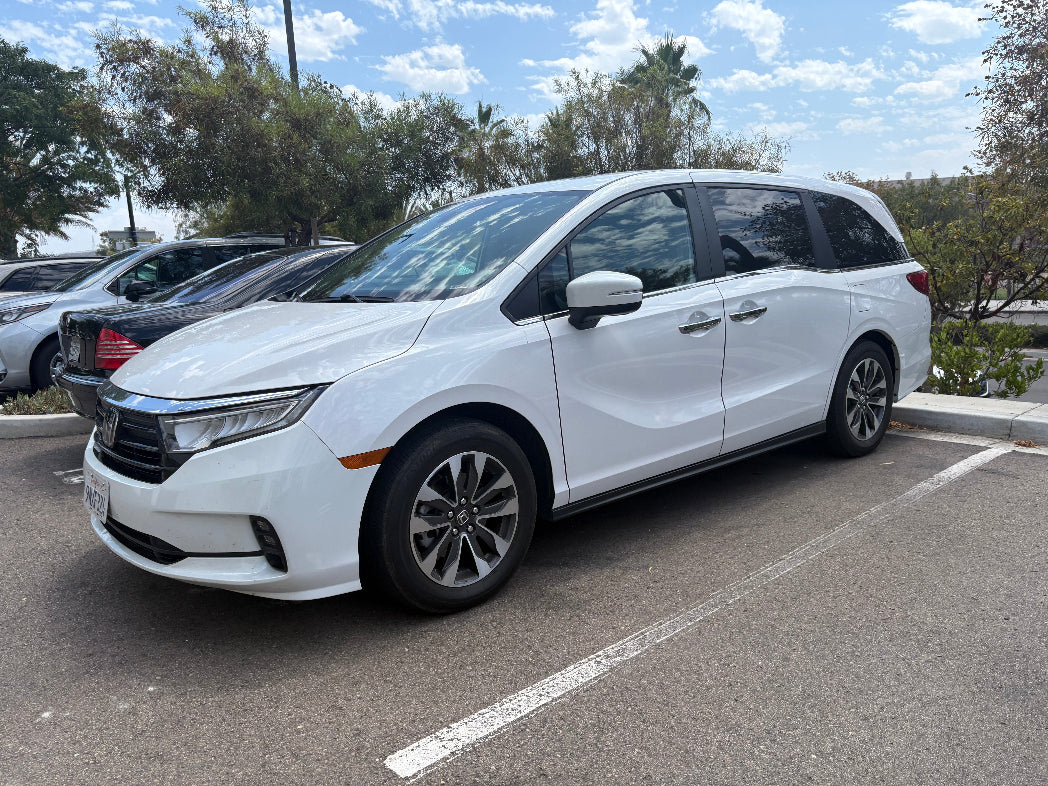 White minivan parked in a lot with trees and other vehicles in the background