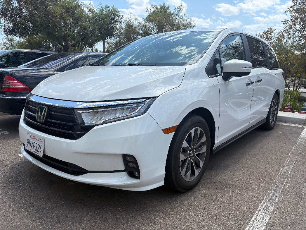 White Honda minivan parked in a lot with trees and sky in the background