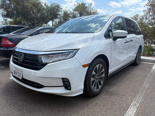 White Honda minivan parked in a lot with trees and sky in the background