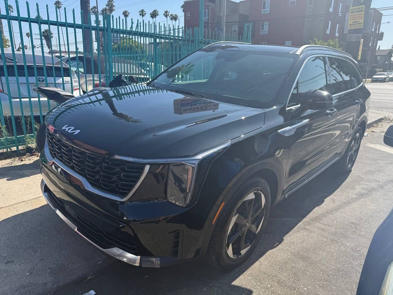 Rental Kia SUV parked on a street with a fence and buildings in the background