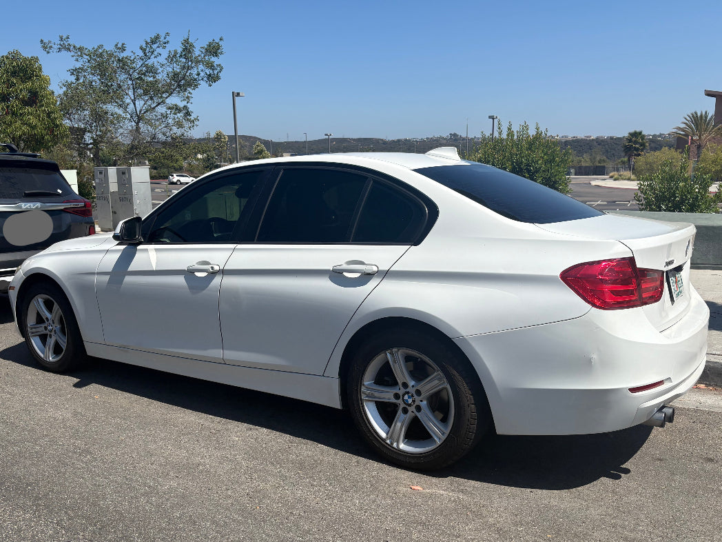 White BMW car parked on a paved surface with trees and clear sky in the background