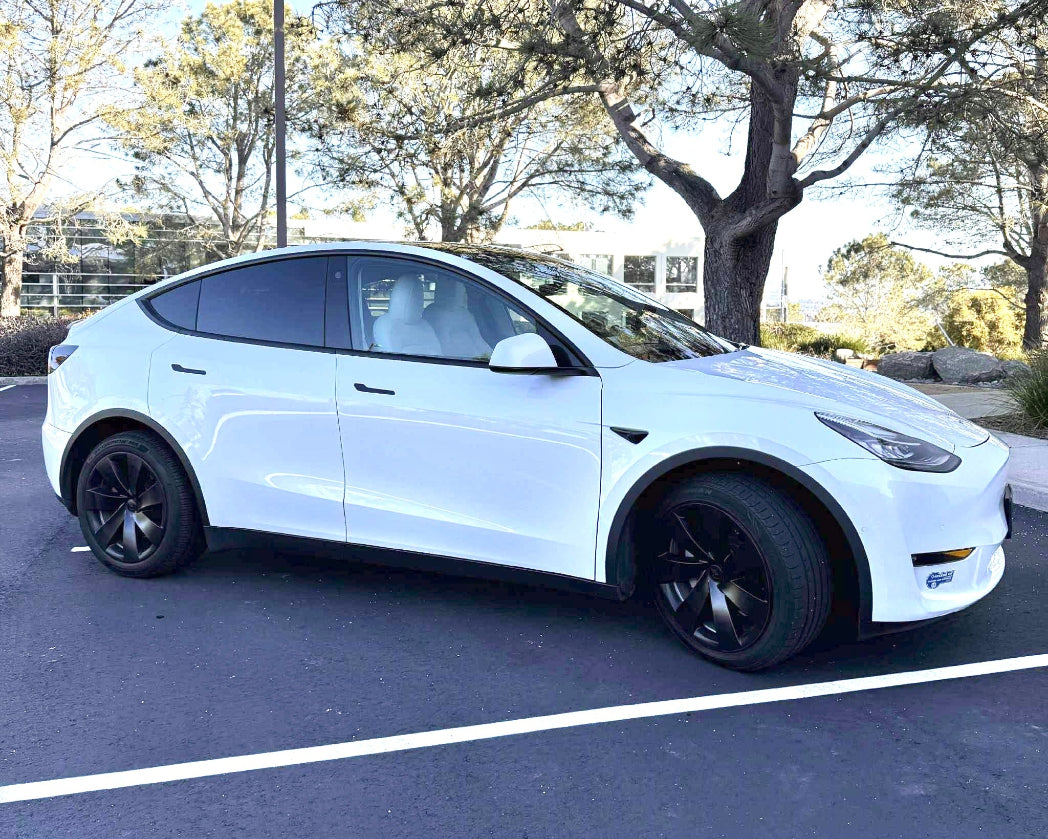 White Tesla Model Y parked on a paved surface with trees in the background