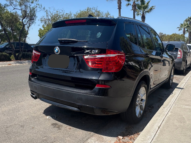Black BMW X3 parked on a street with palm trees in the background