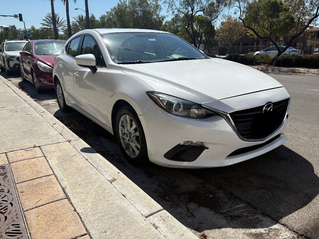 Rental Mazda car parked on the side of a street with trees and other cars in the background.