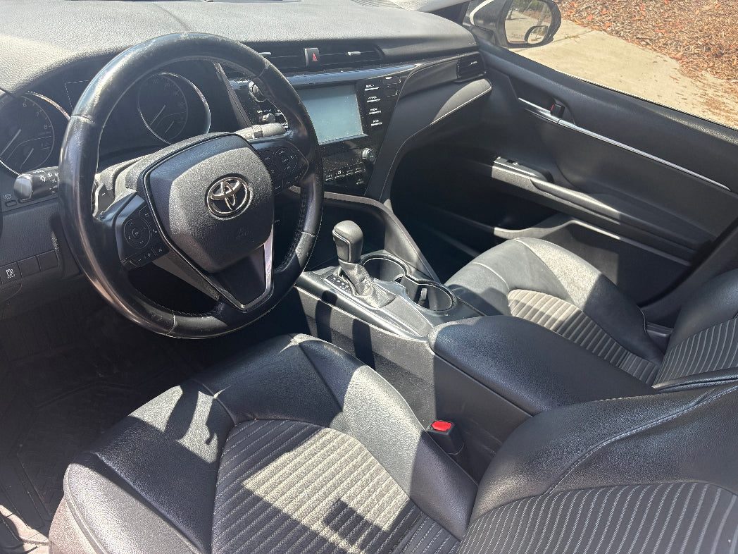 Car interior with steering wheel and dashboard showing Toyota logo.