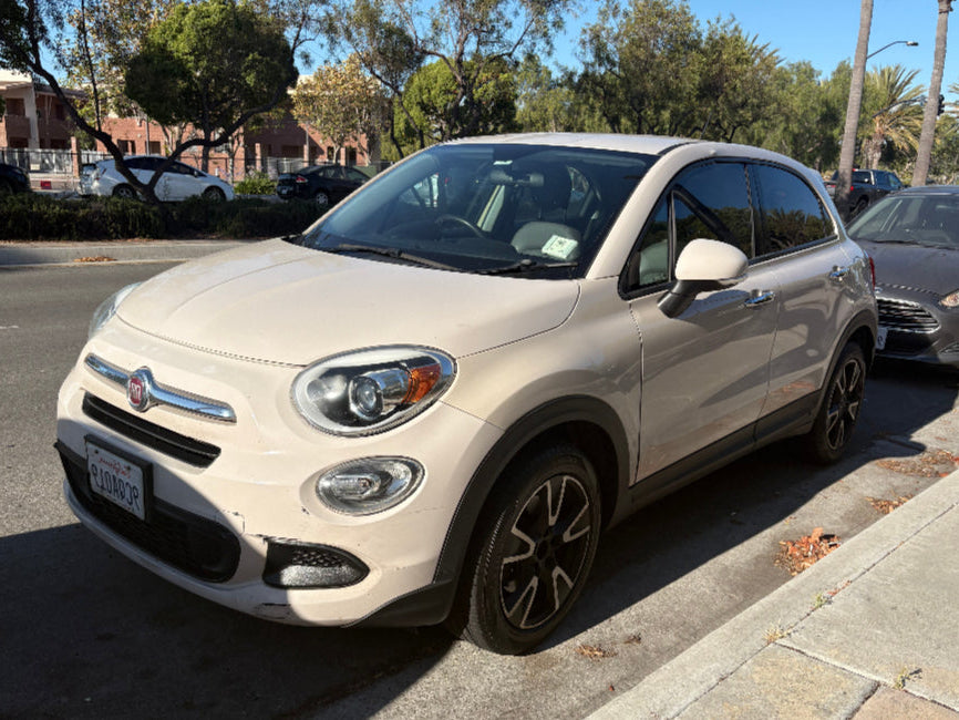 White Fiat 500X parked on a street with trees and buildings in the background