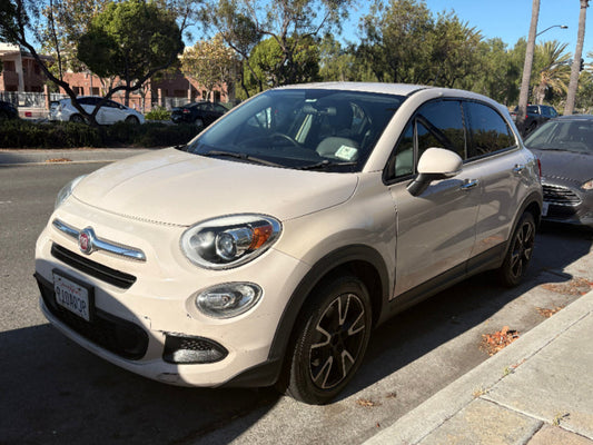 White Fiat 500X parked on a street with trees and buildings in the background