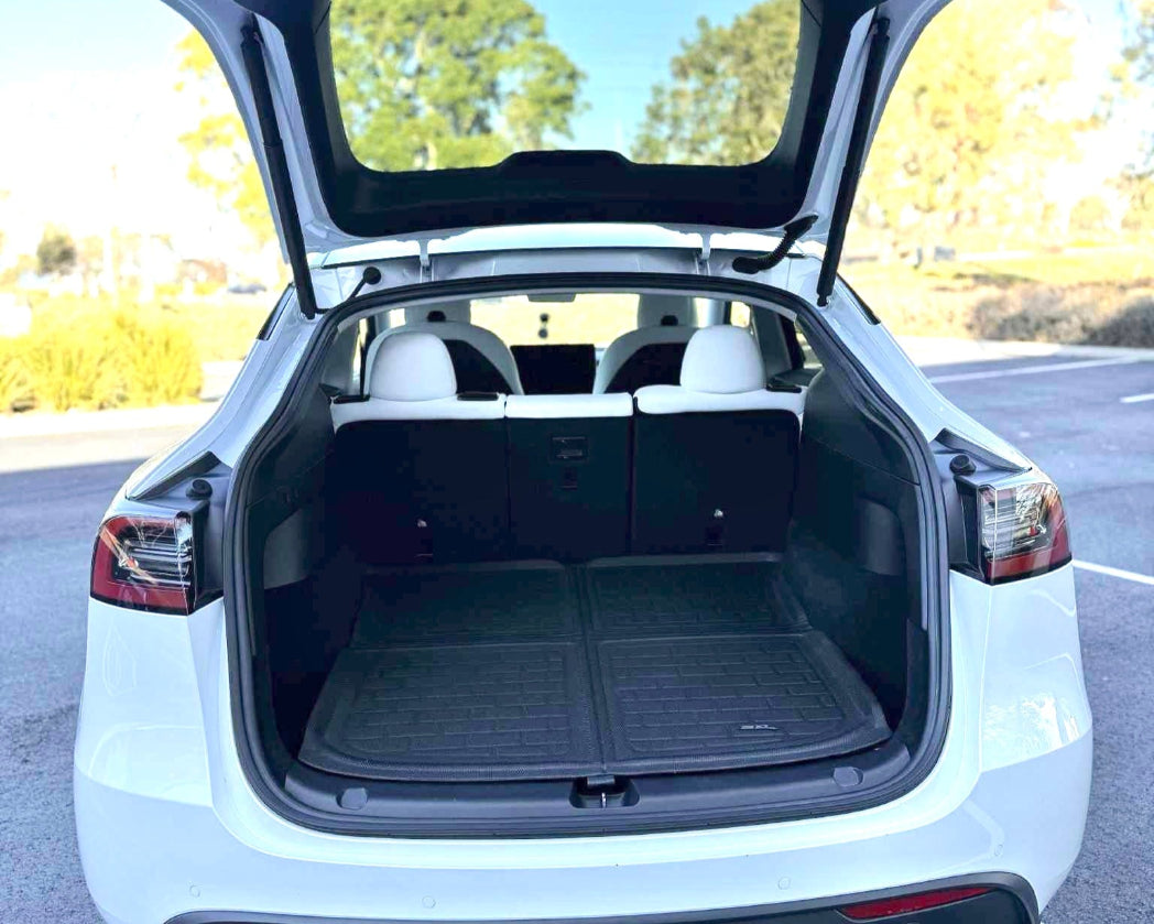 Open trunk of a white car with a clear sky and trees in the background