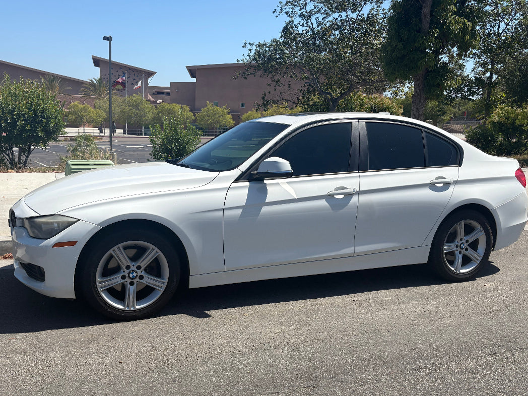 White car parked on a street with buildings and trees in the background