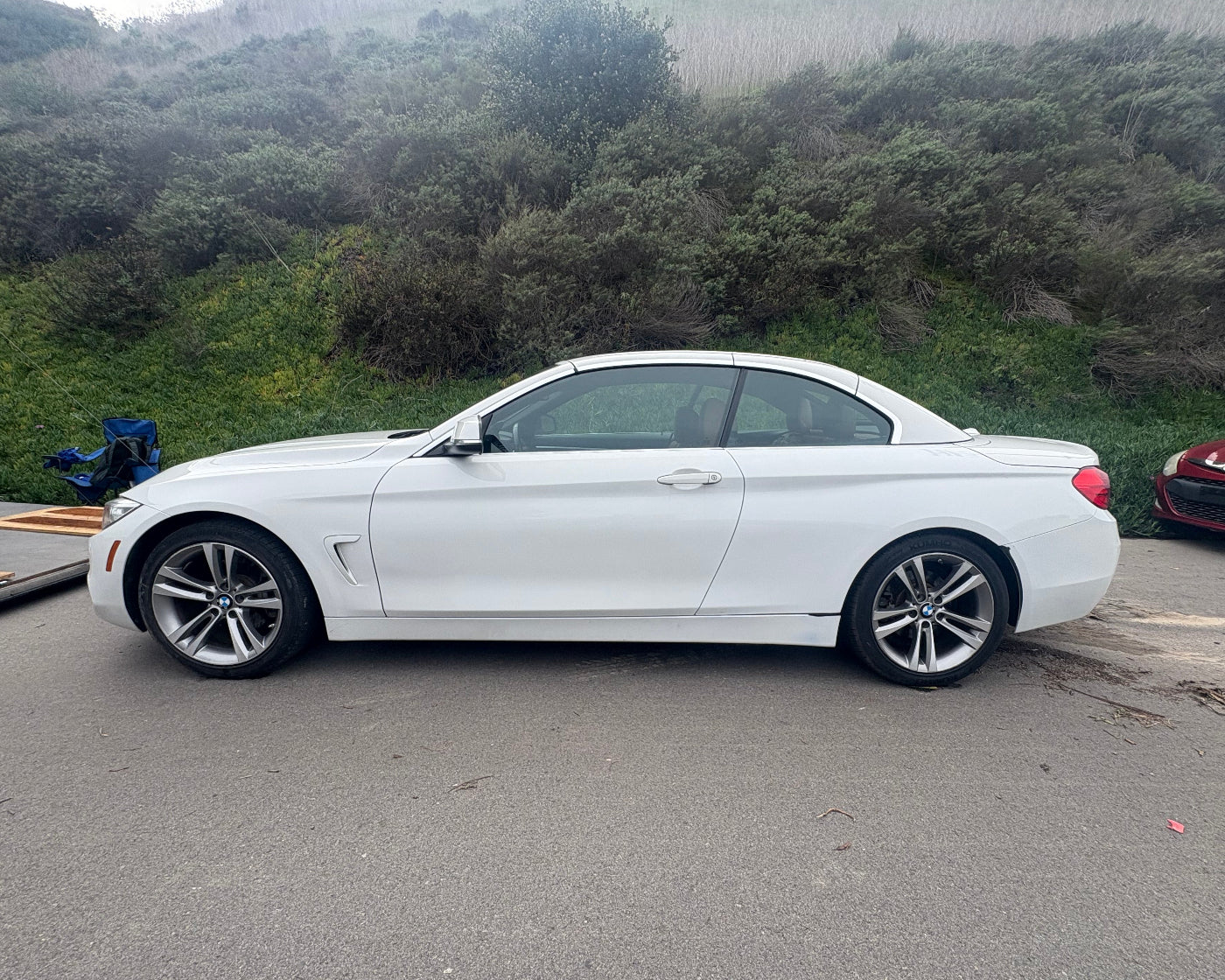 White convertible car parked on a road with a forested area in the background