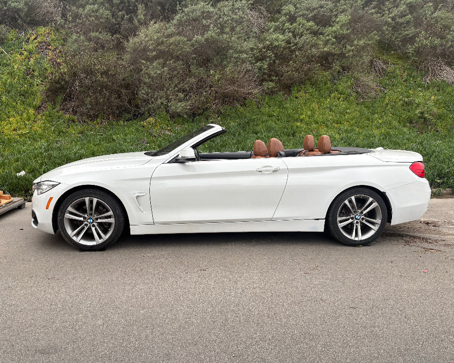 White convertible car parked on a road with greenery in the background