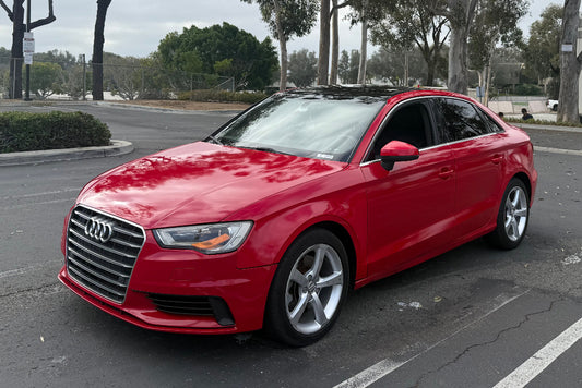 Red Audi car parked on a street with trees in the background