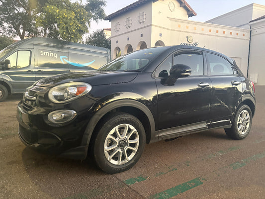 Black Fiat car parked in front of a building with a Prime van in the background.