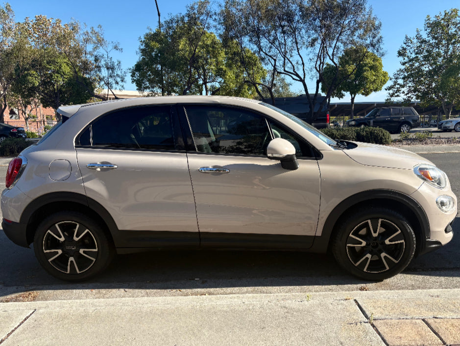 Beige SUV parked on a street with trees and buildings in the background