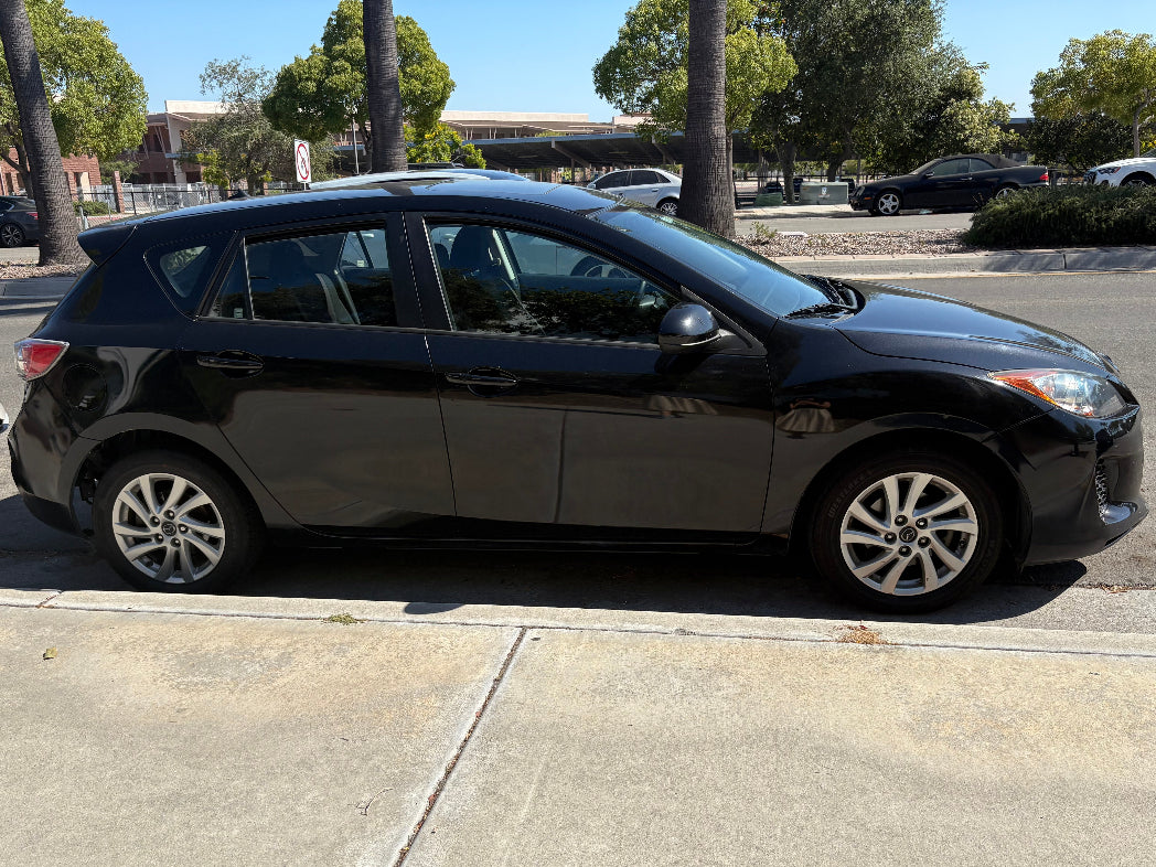 Black car parked on a street with trees and buildings in the background