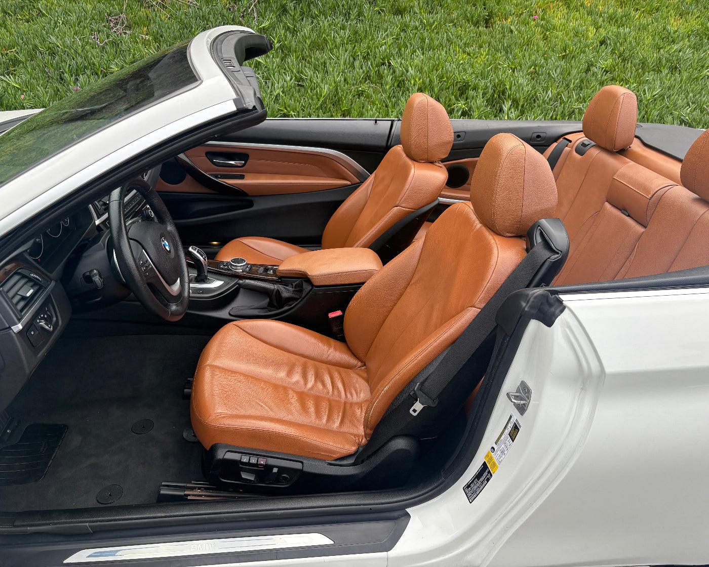 Interior of a convertible car with brown leather seats and a white exterior.