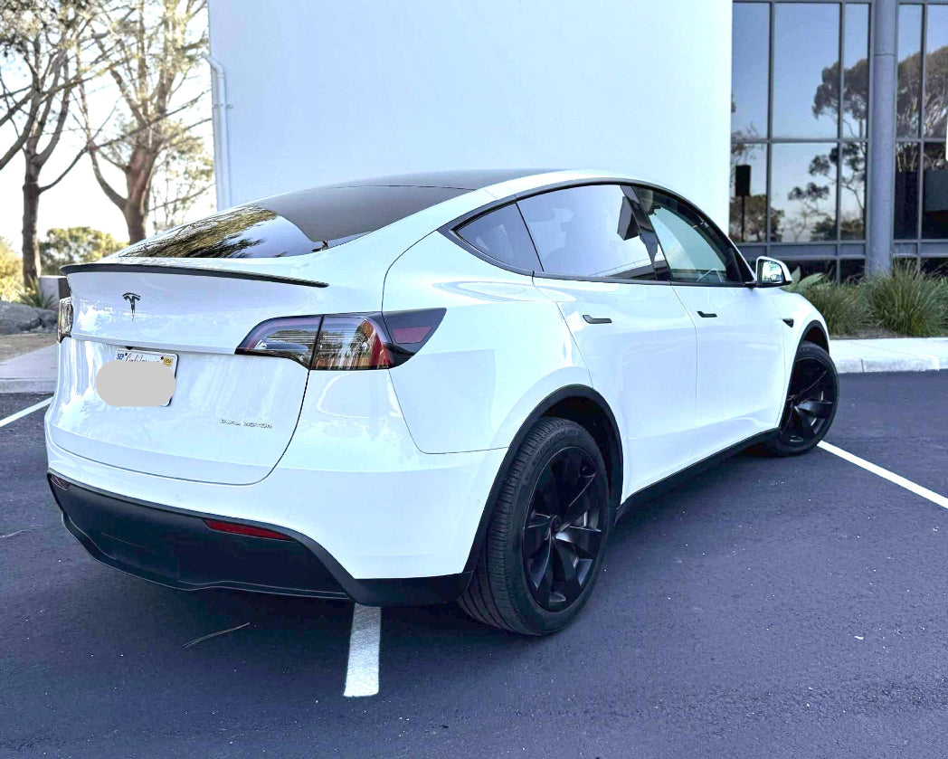 White Tesla Model Y parked in a parking lot with a building in the background