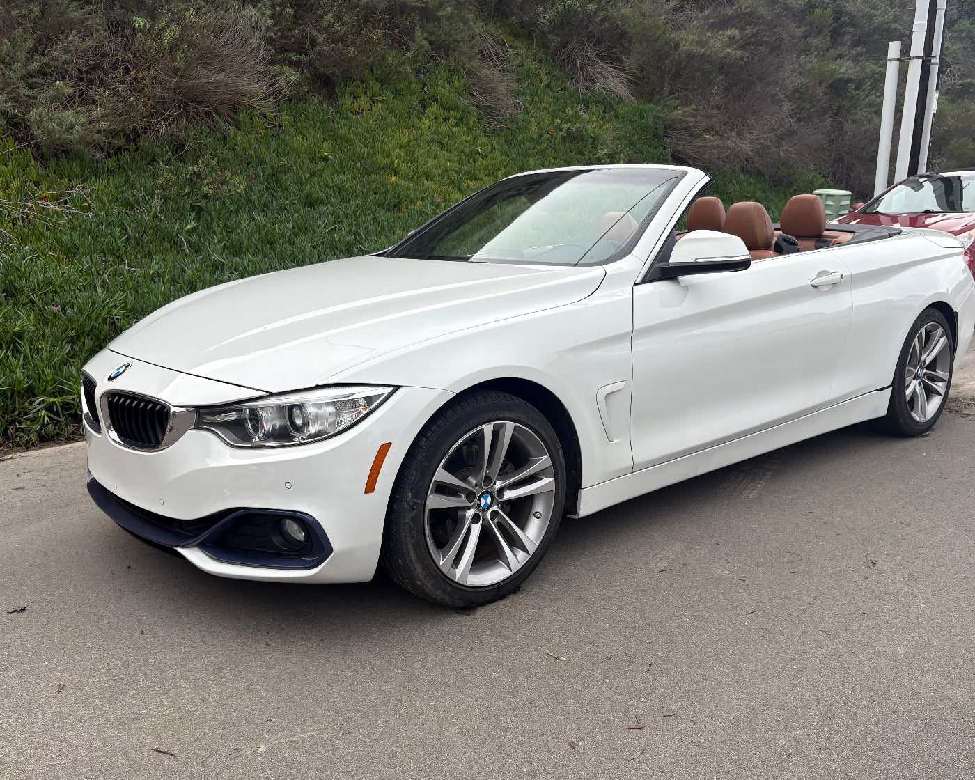 White convertible car parked on a road with greenery in the background