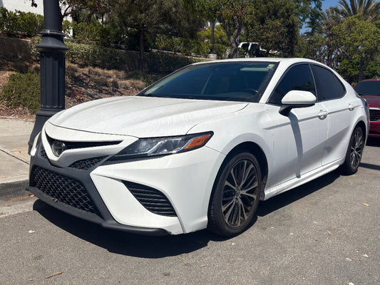 White Toyota for rent in San Diego car parked on a street with trees and a red car in the background