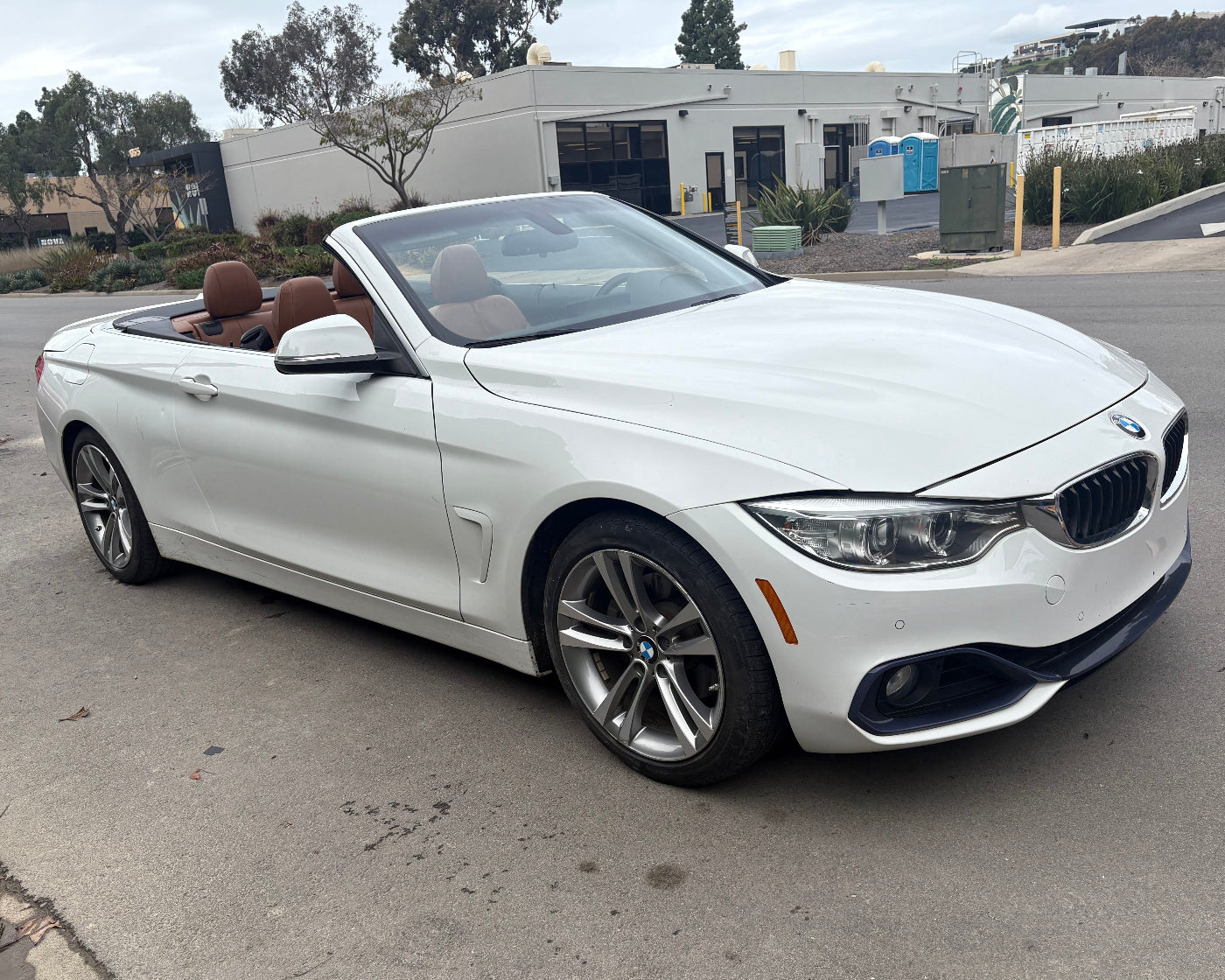 White BMW convertible parked on a street with buildings and trees in the background
