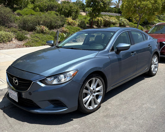Gray Mazda car parked on a street with trees and houses in the background