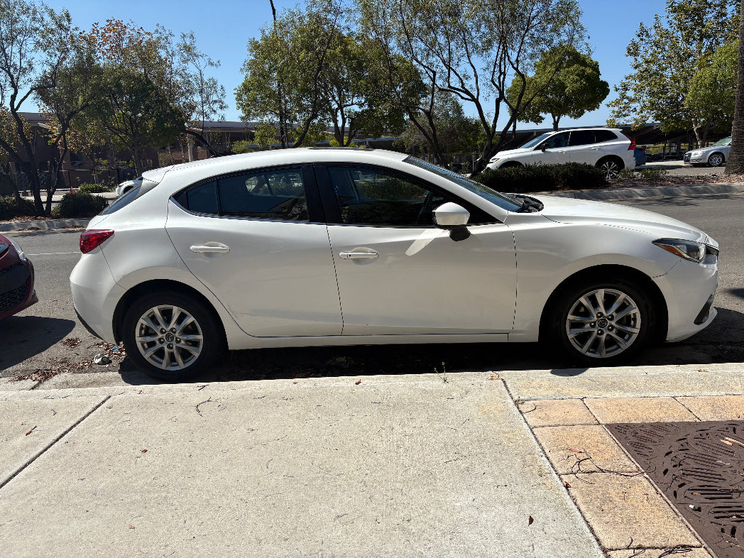 White car parked on a street with trees and buildings in the background
