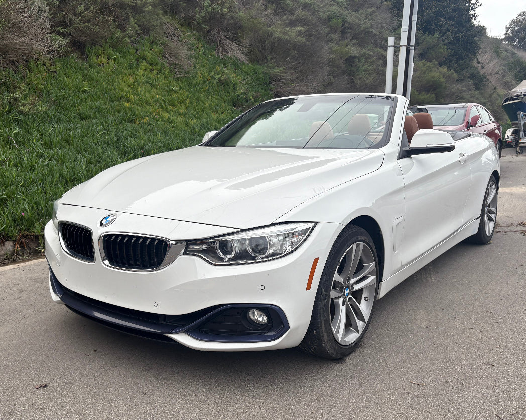 White BMW convertible on a road with greenery in the background