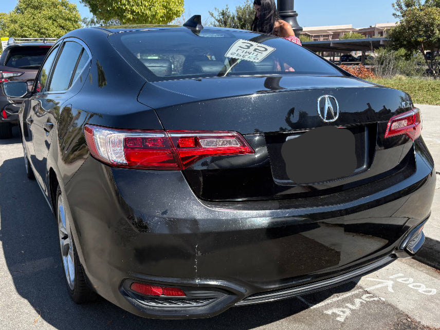 Black Acura car parked in a parking lot with trees and buildings in the background