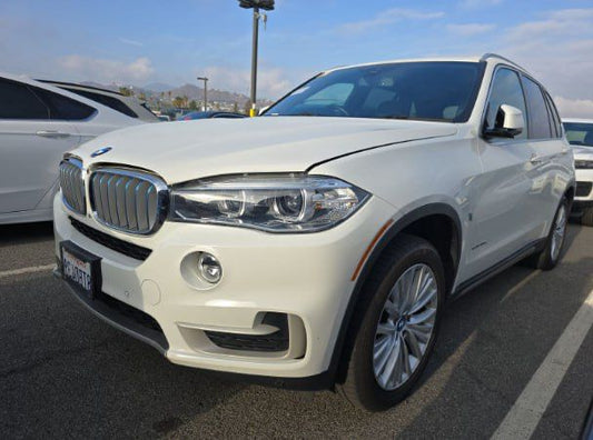 White BMW SUV parked in a lot with other vehicles and mountains in the background