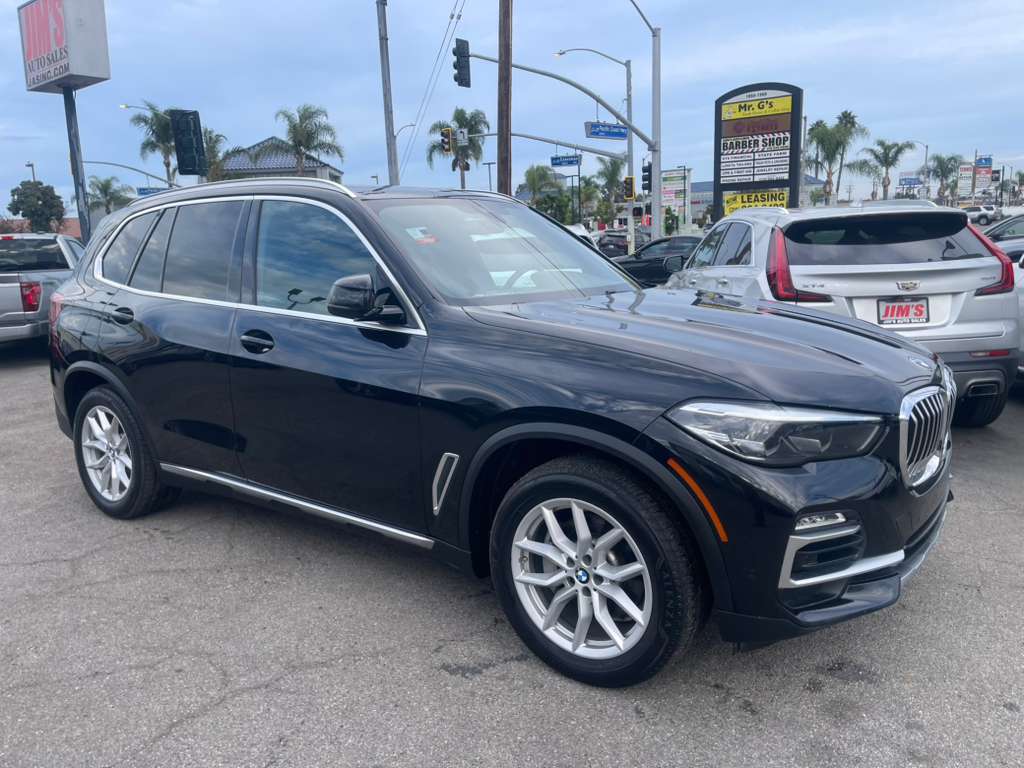 Black BMW SUV parked in a lot with palm trees and signs in the background