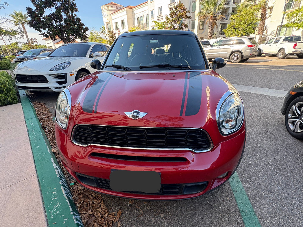 Red Mini Cooper parked on a city street with other vehicles and buildings in the background.