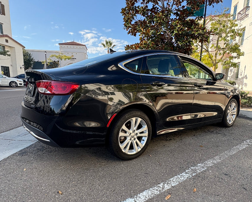 Black car parked on a street with buildings and trees in the background