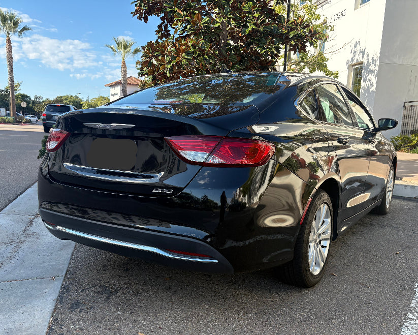 Black car parked on a street with palm trees and buildings in the background